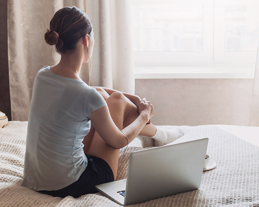 Woman with computer on bed getting ready for teletherapy in NY